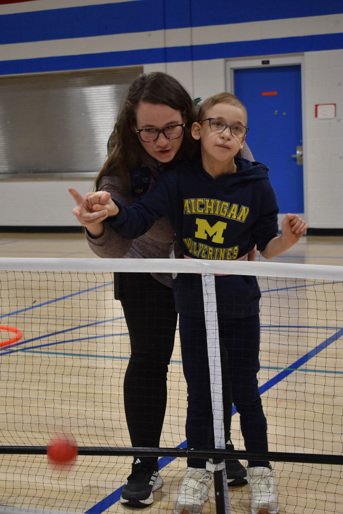 A student throwing the ball with the help of her teacher