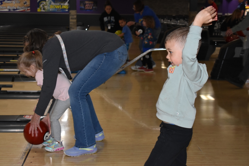 A very excited kid with his hands in the air celebrating after rolling his bowling ball