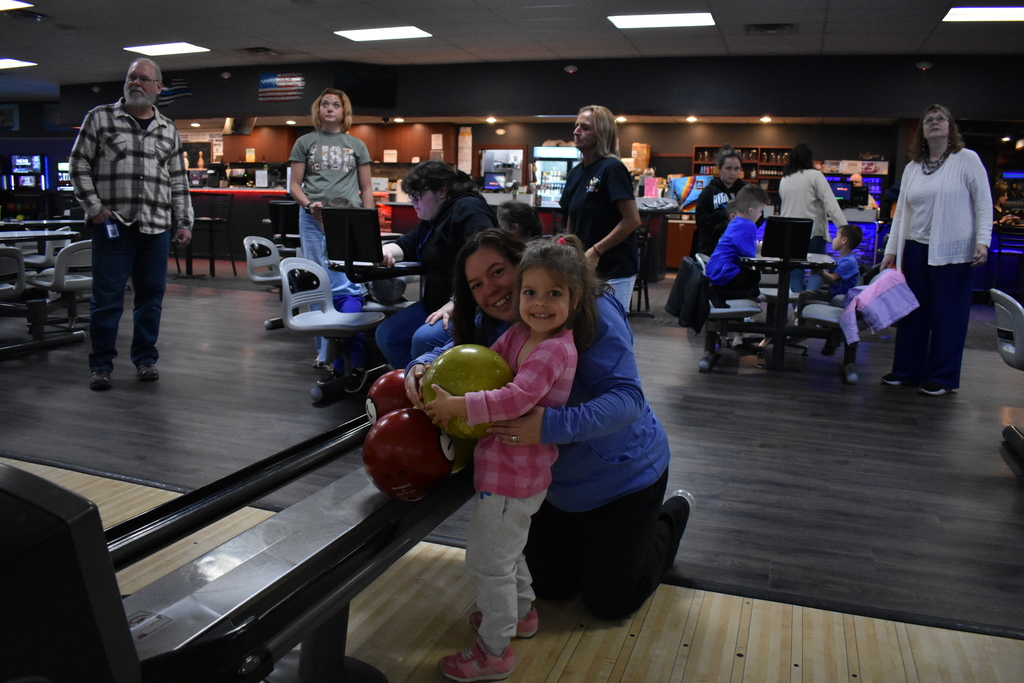 A student and parent smiling at the camera as they pick up the bowling ball