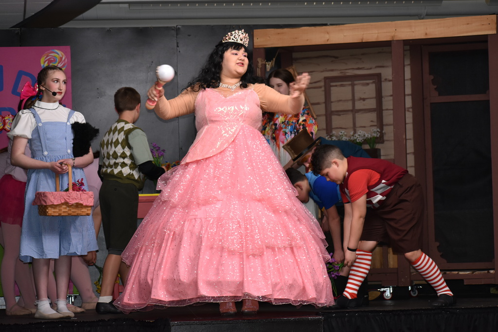 The  good witch singing on stage with other cast dancing near her