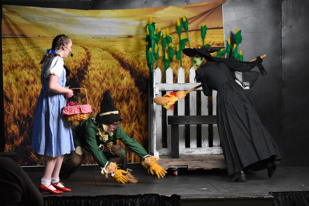 The wicked witch trying to touch the scarecrow with fire as Dorothy looks on