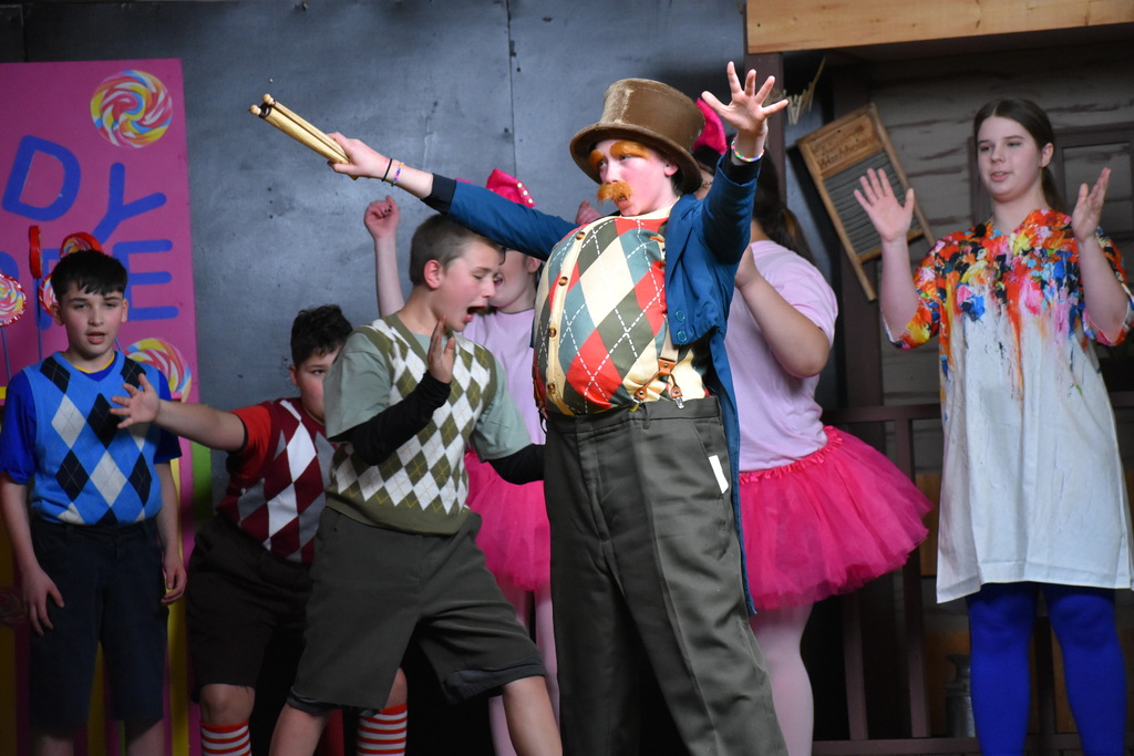 A munchkin singing and dancing while the rest of the cast looks on