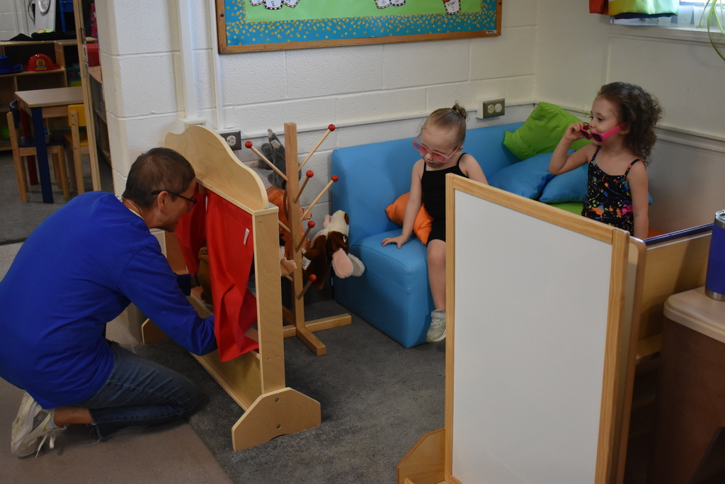 Two children enjoying a puppet show from a teacher