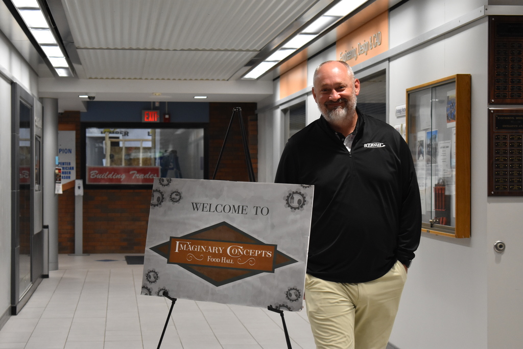 Assistant Principal standing with the Imaginary Concept Food Hall sign