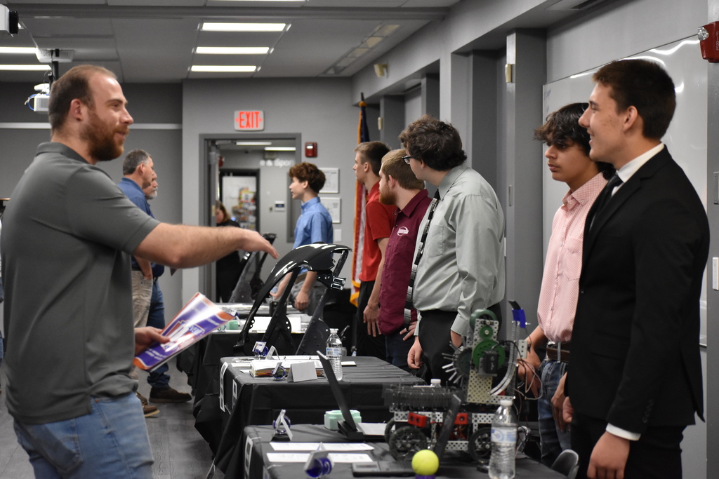 Students speaking to an employer with other participants at tables in the background