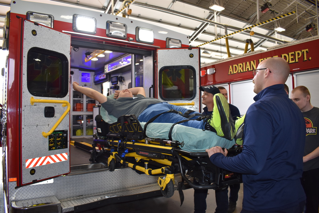 A student acting like a patient while a firefighter puts him in an ambulance