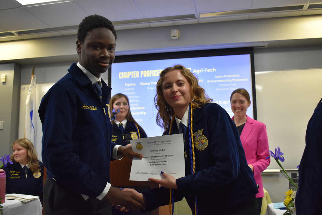 A student receiving an award and shaking the hand of a peer