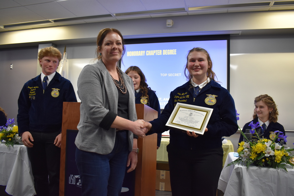 Students giving an award to a volunteer and shaking her hand