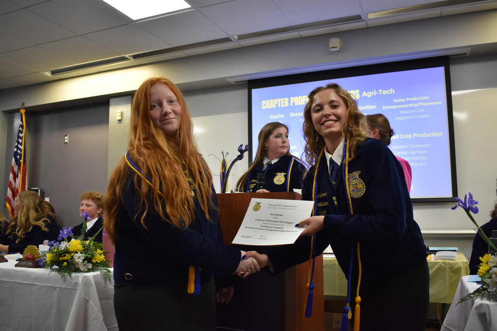 A student receiving an award and shaking the hand of a peer