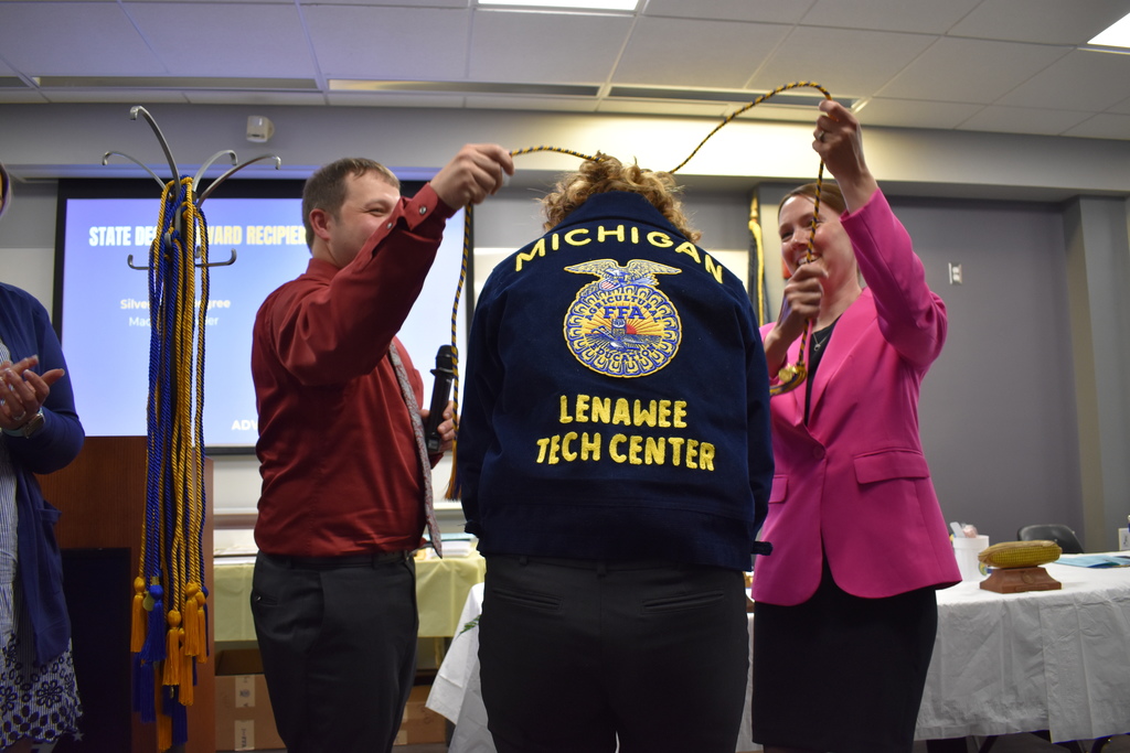 Two instructors placing an excellence cord over a student