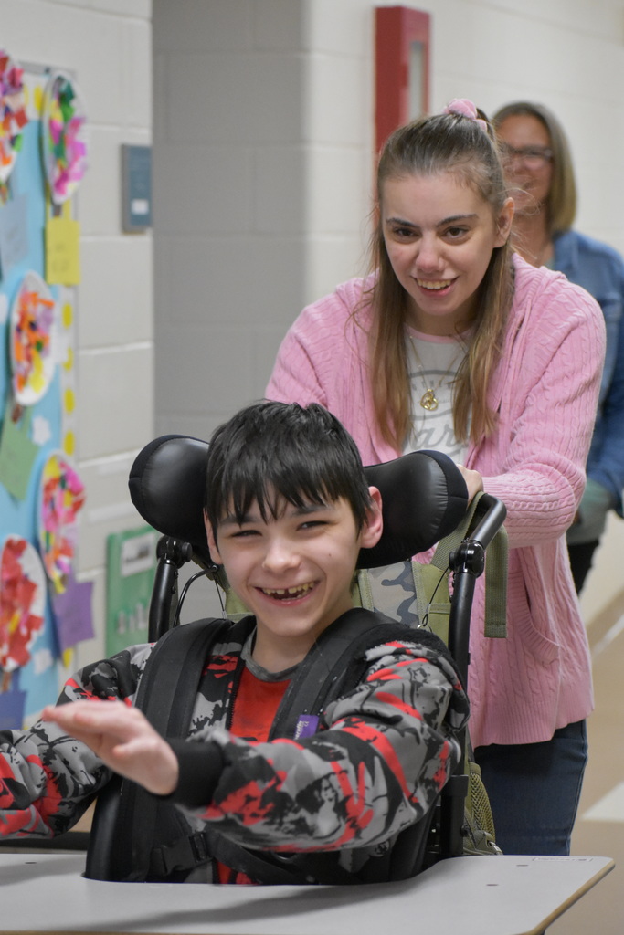 A student being pushed down the hall by a volunteer