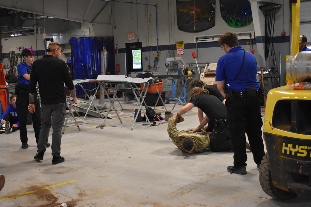 Students arresting a shooter during a demonstration while  a police officer watches to teach and assist