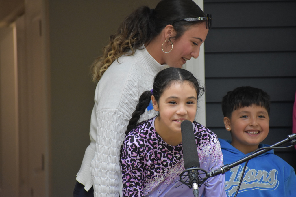 The daughter speaking into the mic while her mom and brother stand behind her