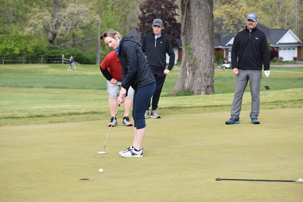 A golfer putting while her team looks on