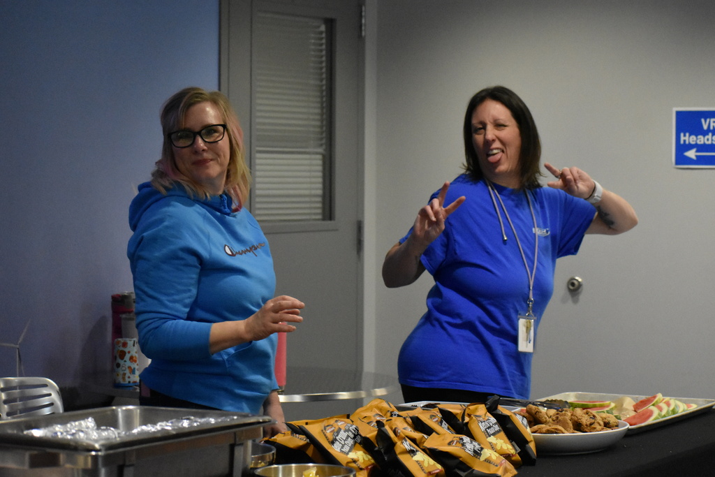 Two staff members smiling at the camera while they serve food to students