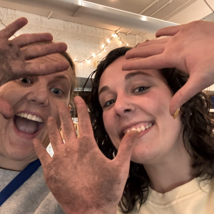 Two teachers smiling at the camera and showing their dirty hands from working in the garden