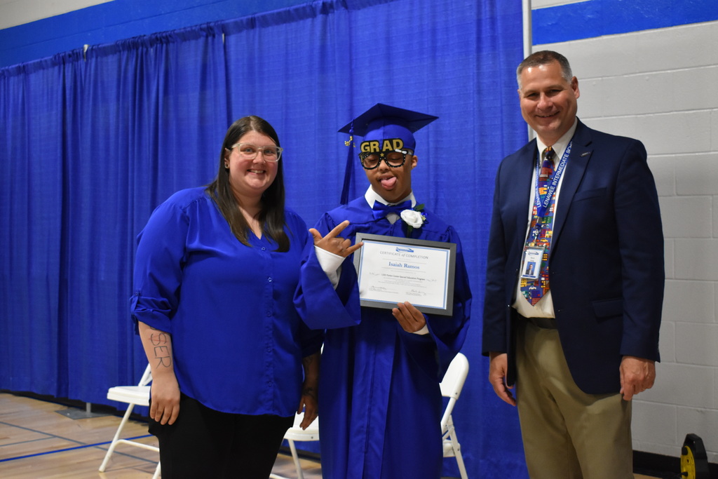 A graduate with his diploma and two staff members