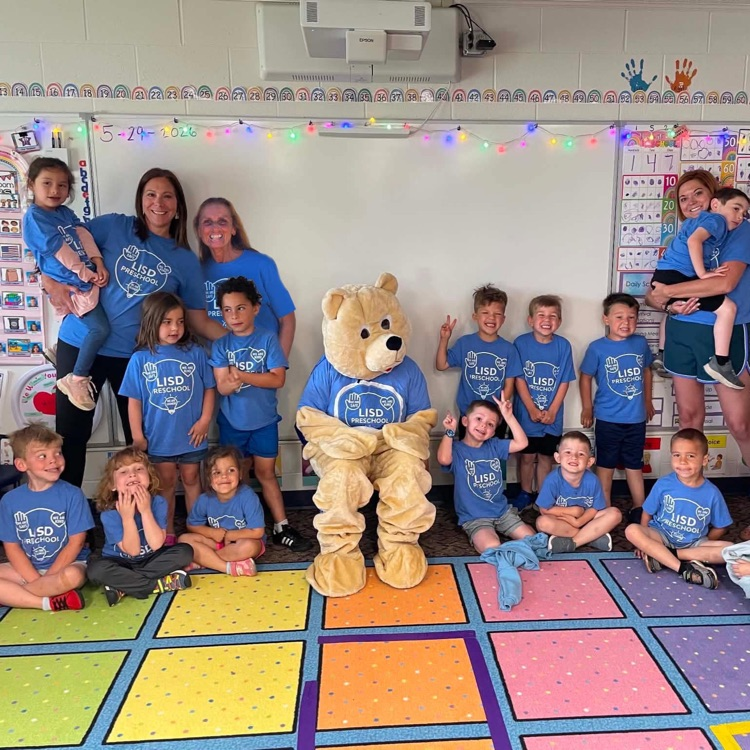 a classroom photo of students and teachers, along with their bear mascot  