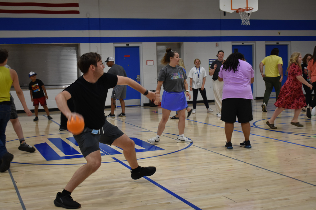 A teacher throwing a ball during a game of Castle Ball in a gym full of students and staff