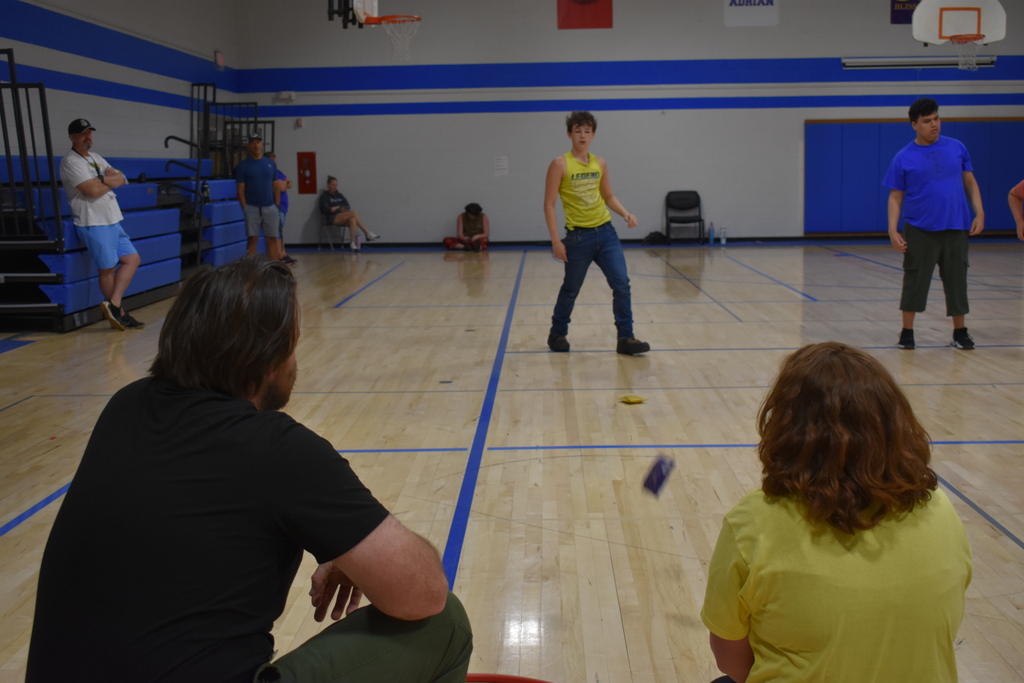 A student throwing a bean bag into a hoop, while teachers look on