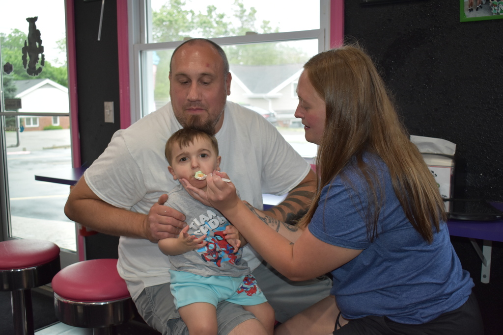 A young child eating ice cream with the assistance of his family