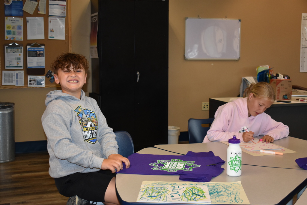 A student smiling at the camera while he works on a shirt design