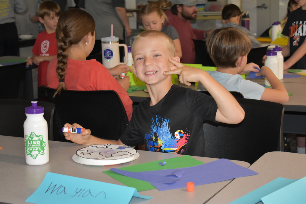 A kids smiling at the camera giving the peace sign