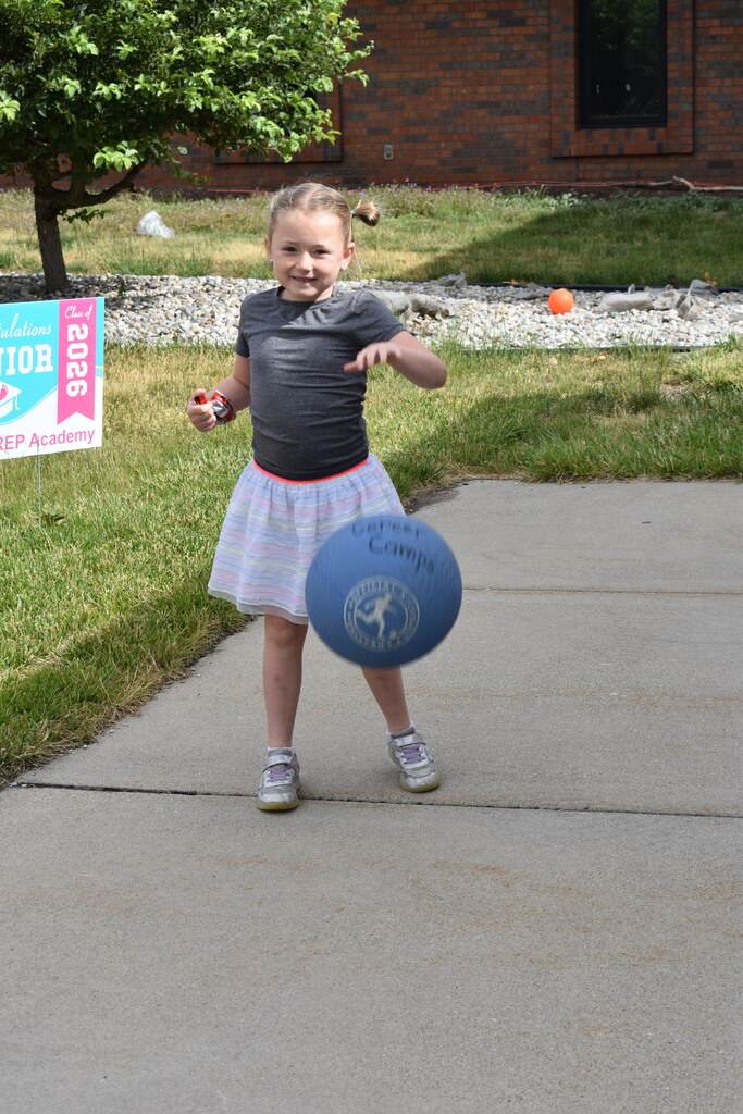 A young girl dribbling a ball on the sidewalk and smiling at the camera