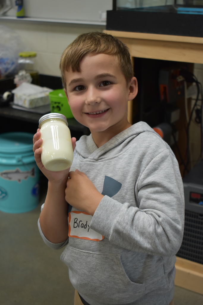 A young student smiling at the camera with his jar of butter