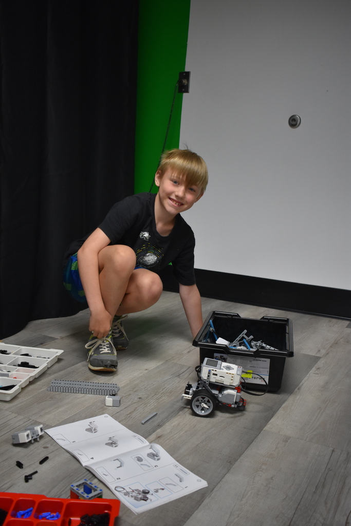 A student building a robot and smiling at the camera