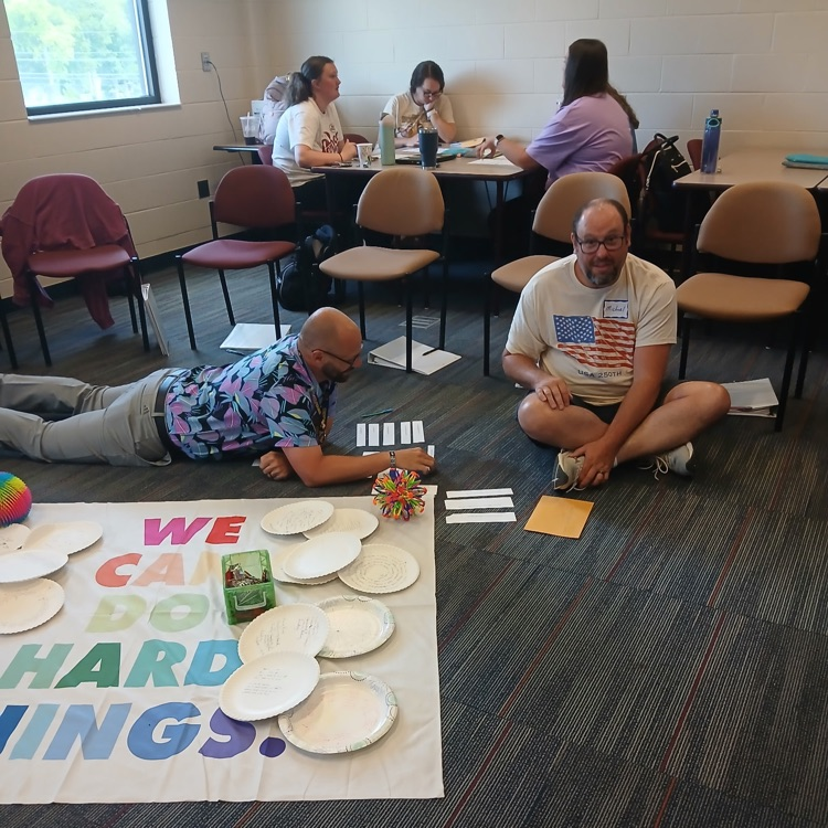 two staff members working on the ground with paper plates while others work at a table behind them 
