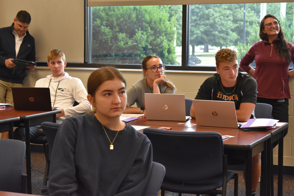Students at desks and a staff member standing behind them