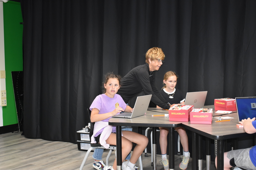 Two students working at their table while the teacher assists