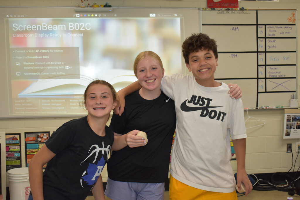 Three students smiling at the camera and holding their butter they are making