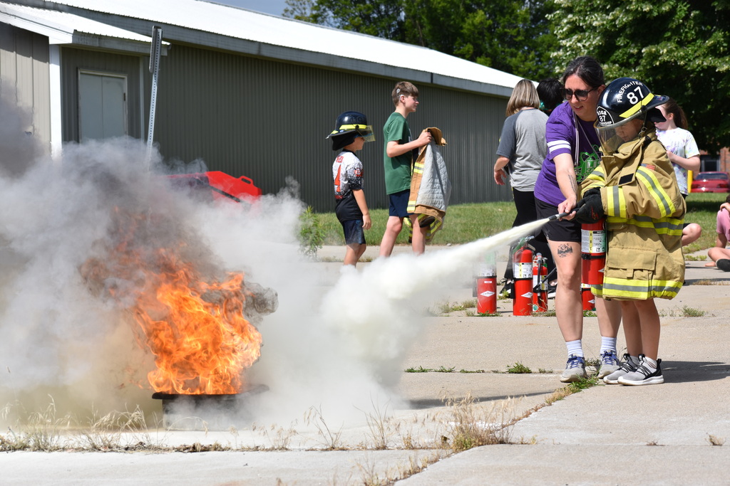 A kid putting out a fire while a teacher assists