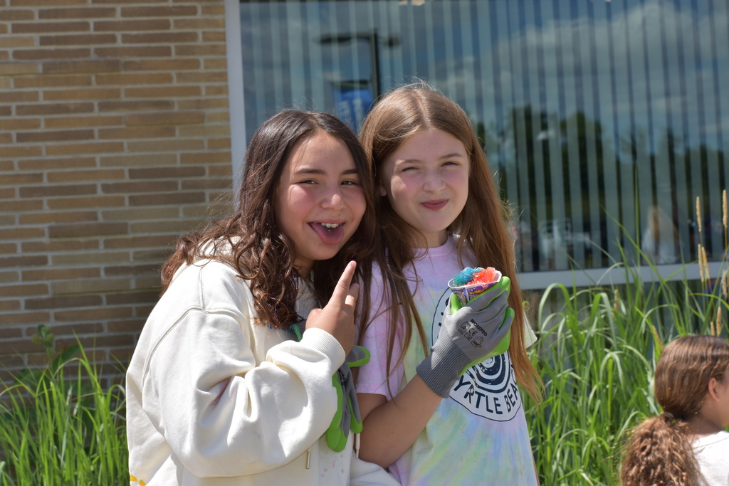 Two girls smiling at the camera while one gives a peace sign and the other eats a snow cone. 