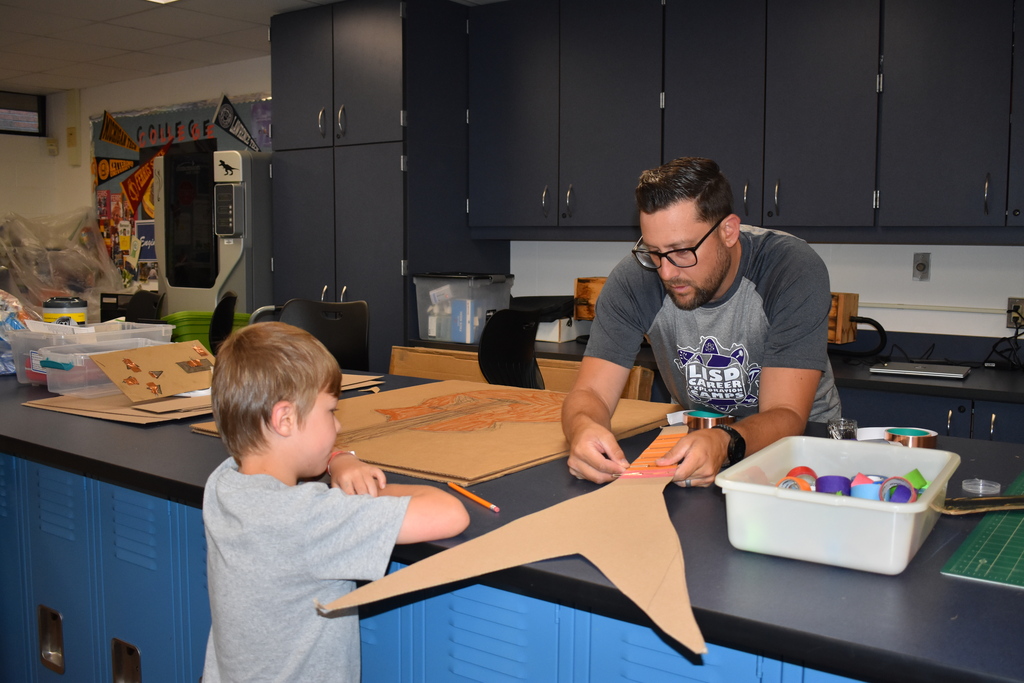 A teacher helping a student with his cardboard instrument