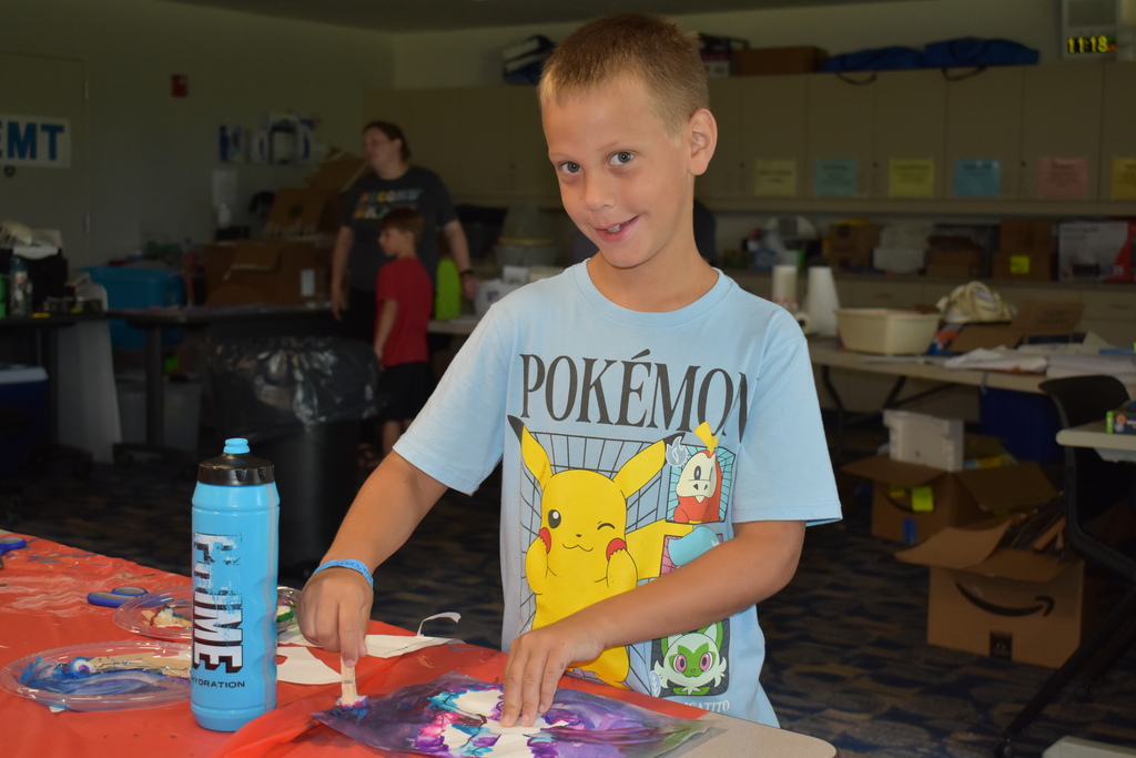 A young boy painting and smiling at the camera