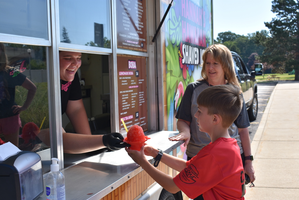 Hannah's Hawaiian Shaved Ice handing a student an icee while an adult looks on