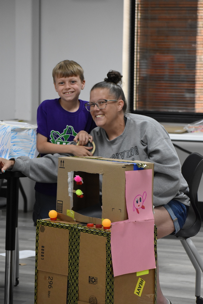 An adult and kid smiling at the camera with the game they made