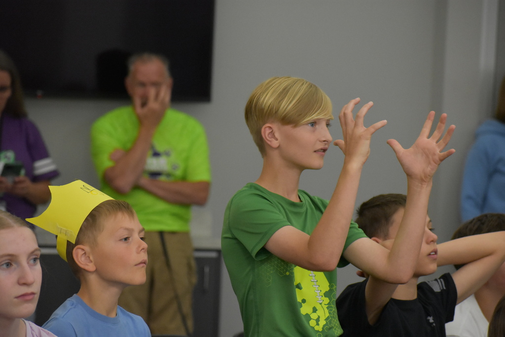 A kid in the crowd standing and making a hand motion as he watches a science experiment