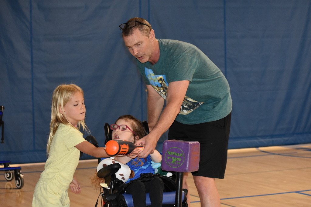 A teacher and young girl helping a student swing the bat