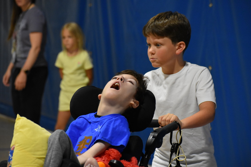 A young boy pushing a student in his mobility device around the bases