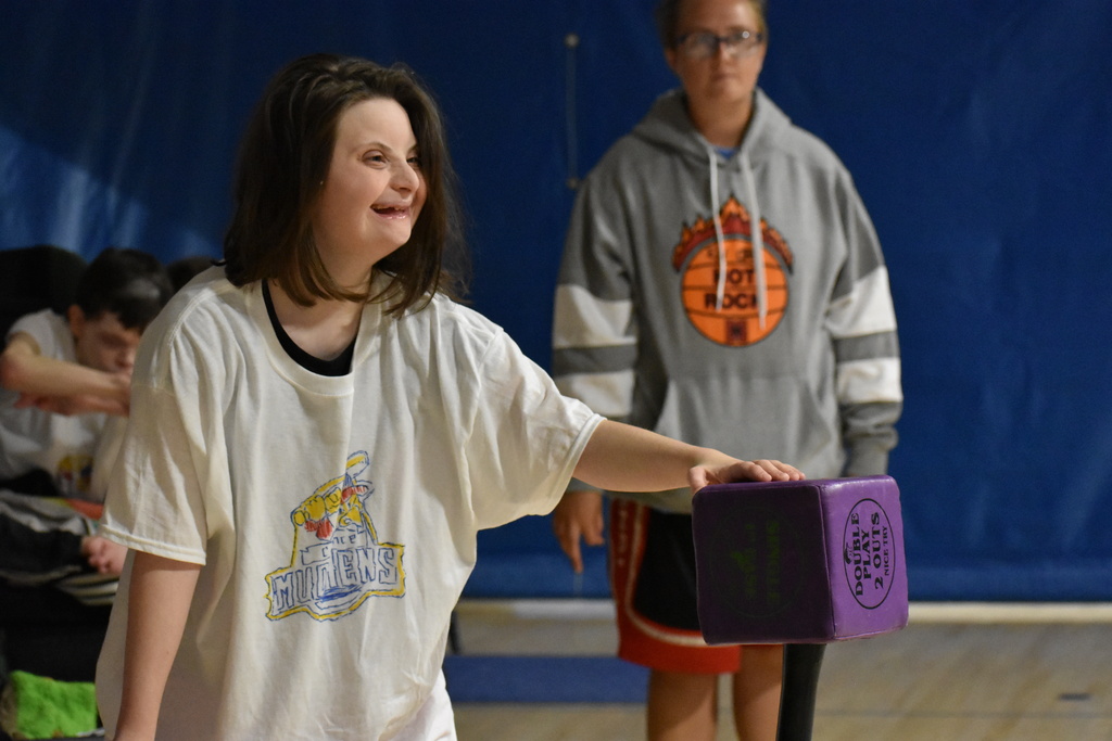 A student hitting the cube for adaptive baseball while a staff member looks on in back