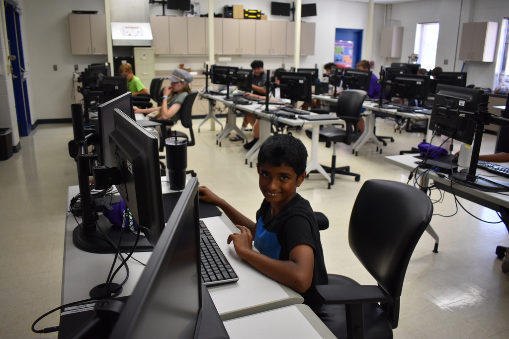 A young student at a computer working and smiling at the camera