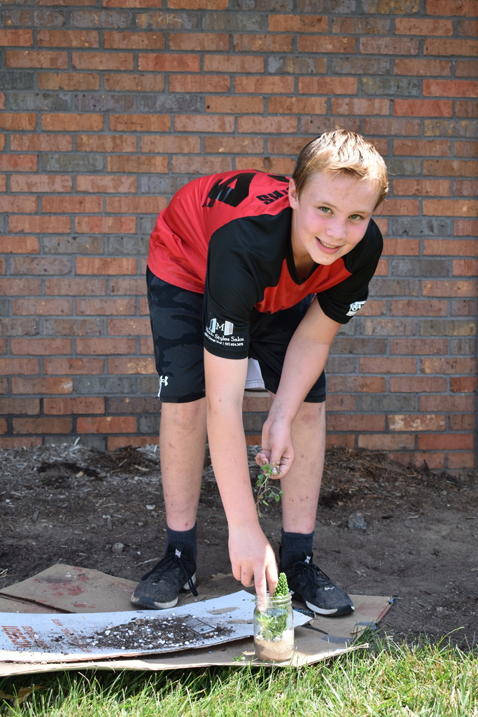 A student bending over to pick up his project off the ground outside