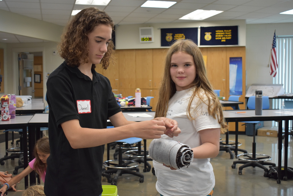 Two young students helping each other wrap their plant