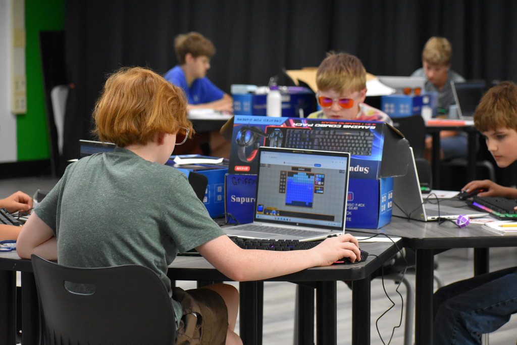 A student on a computer working on a game creation with others in the background doing the same