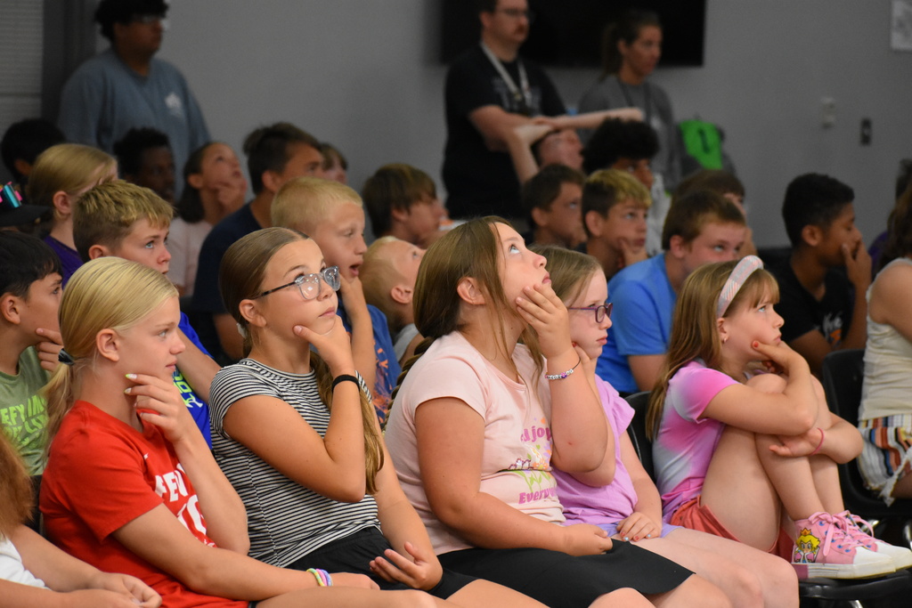 Students in a crowd holding their jaws and moving their eyes to mimic an owl