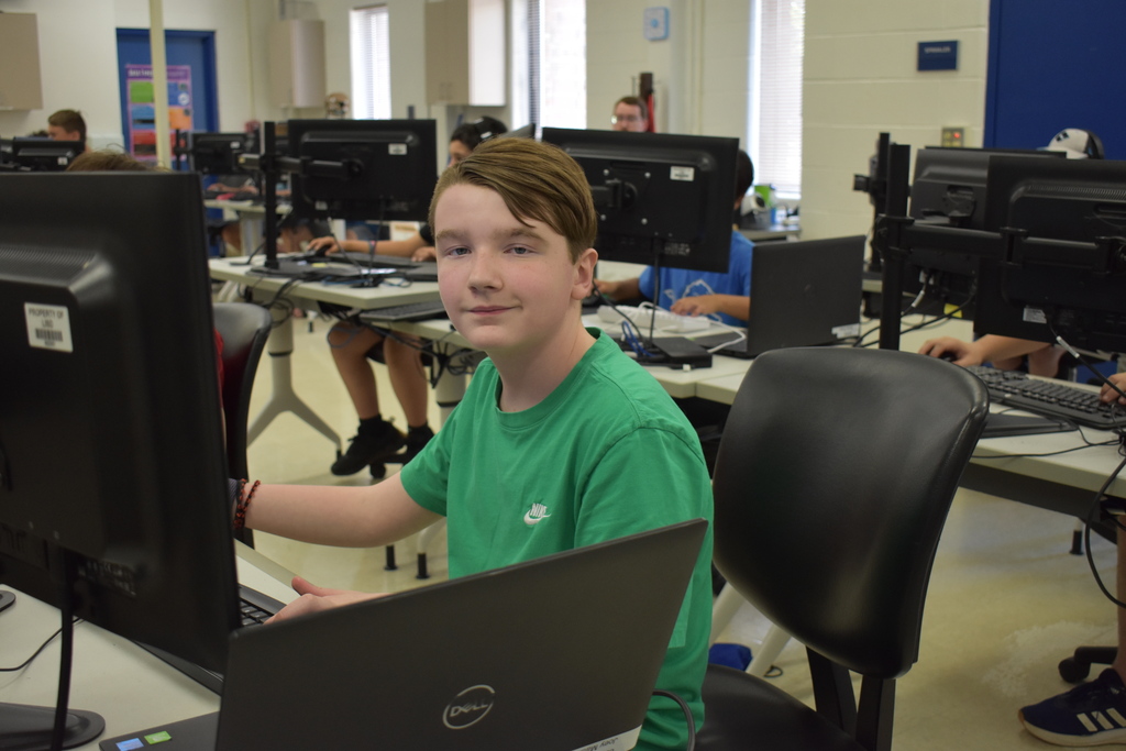 A student smiling at the camera while working on a computer